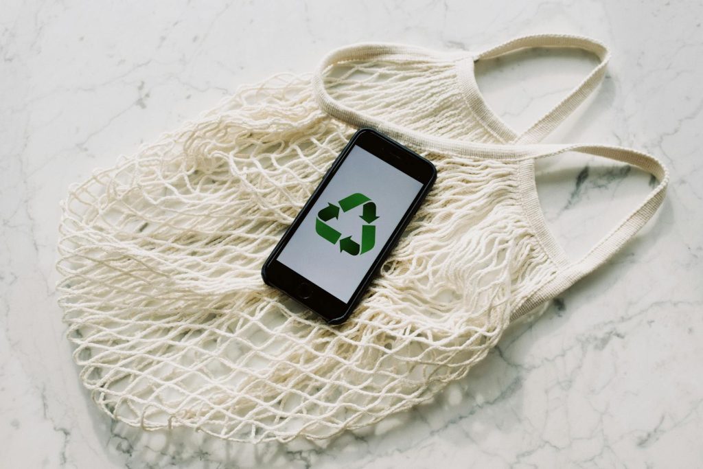 Overhead of smartphone with simple recycling sign on screen placed on white eco friendly mesh bag on marble table in room - eco-friendly cosmetic packaging