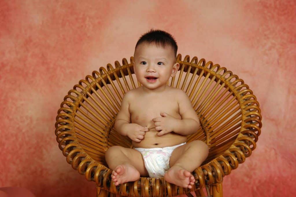 Baby Sitting on Brown Round Bamboo Chair - Organic Diapers