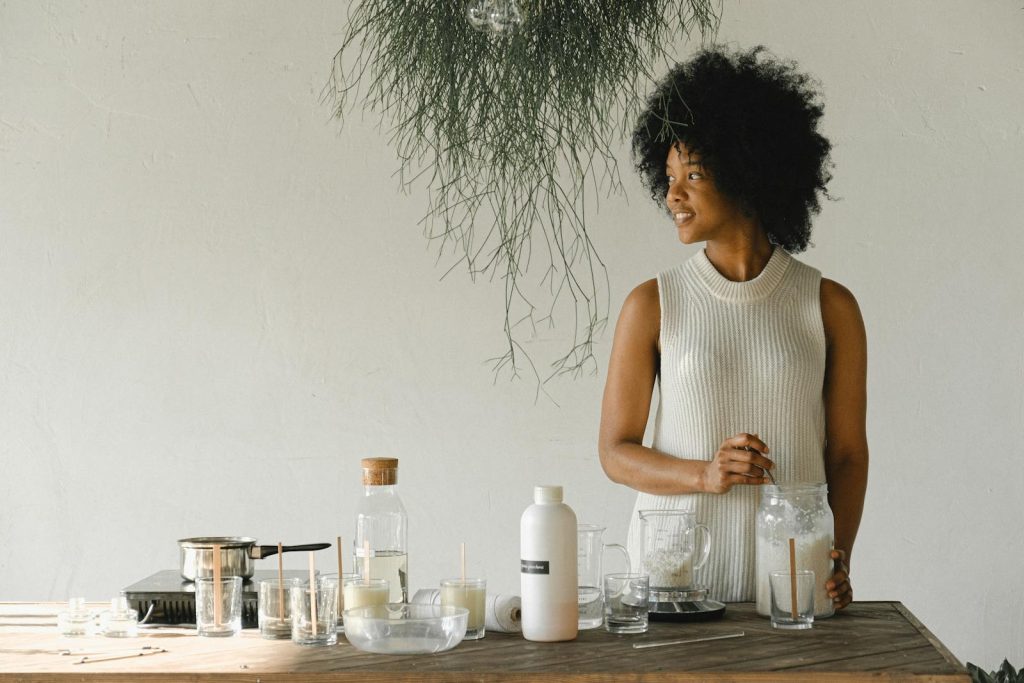 Content African American female artisan with jar of wax flakes looking away while creating candles in modern workshop in light room - natural facial moisturizers