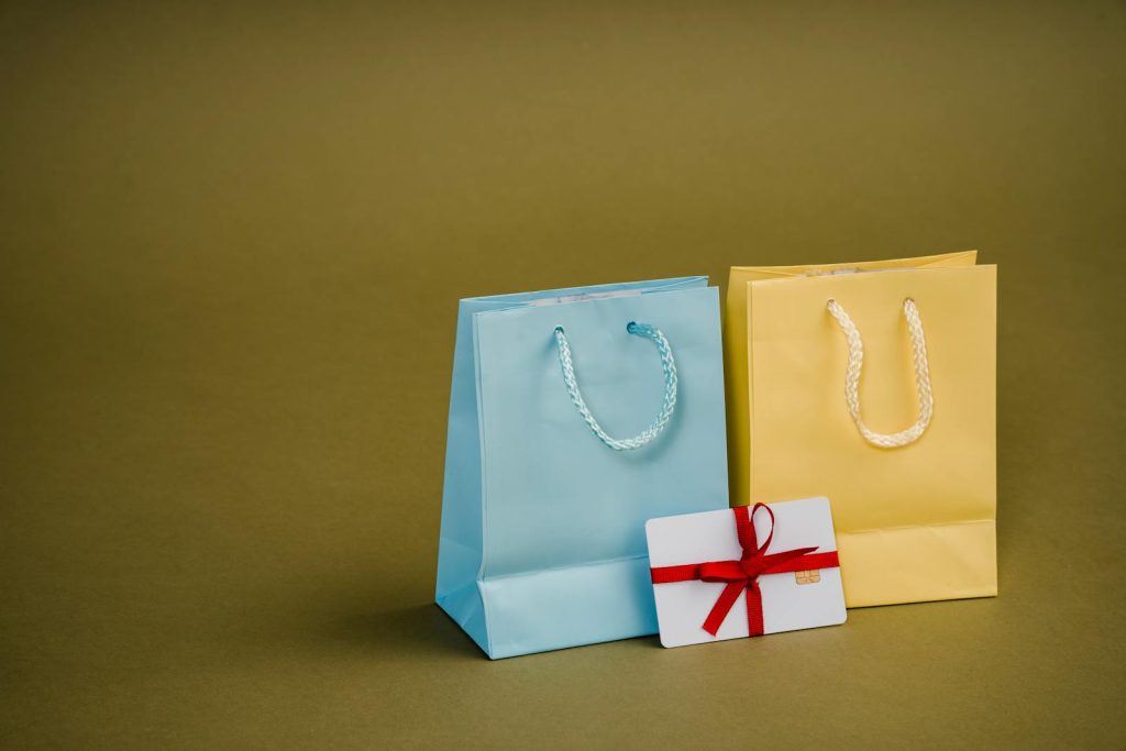 Collection of bright present paper bags with natural handles near gift card with ribbon - eco-friendly packaging for cosmetics
