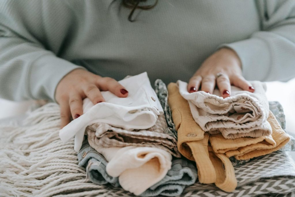 Crop faceless female with manicure arranging baby clothes on warm scarf while sitting at table in light room at home - Is Polyester Plastic?